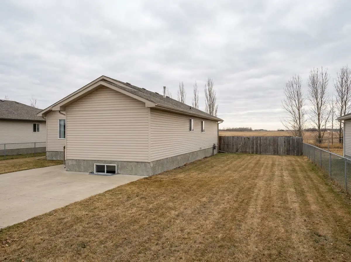 A 1990s Airdrie bungalow on a wide flat lot, with an open grassed side yard giving machine access from the driveway to the foundation.